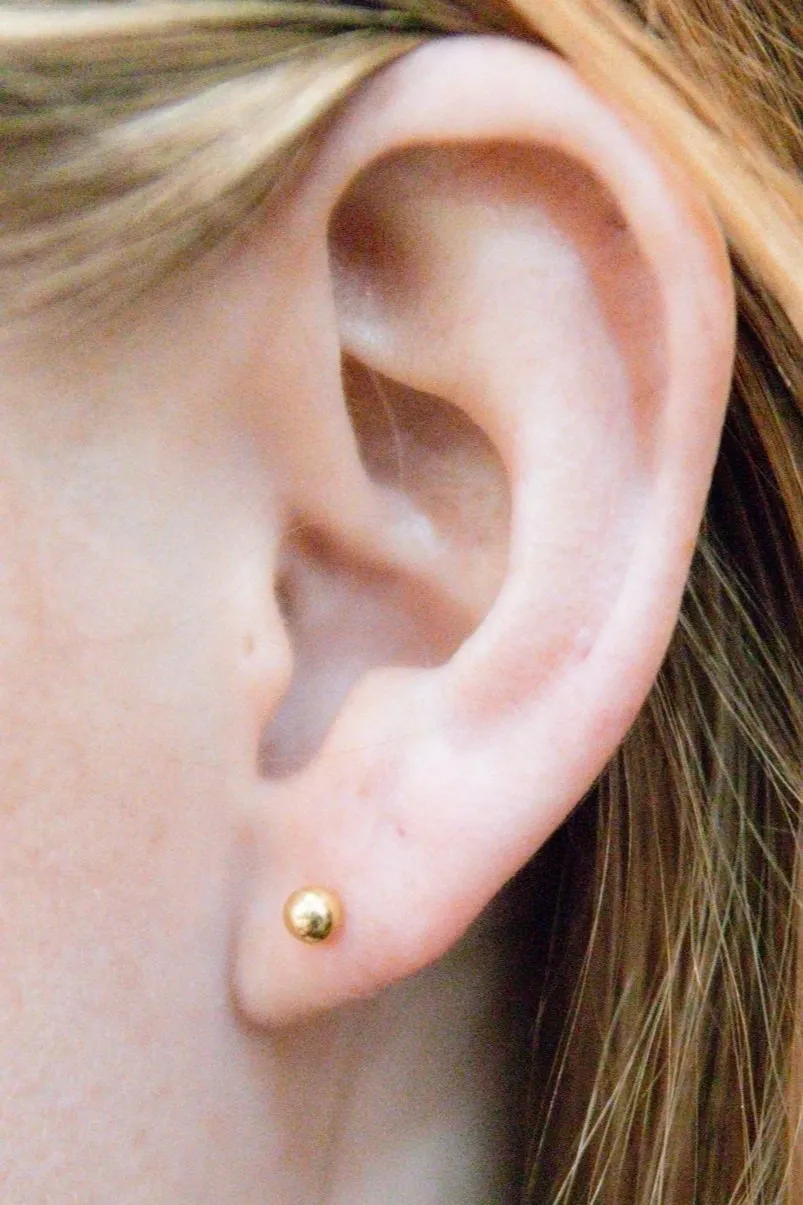 A woman 's ear with a gold earring on it.