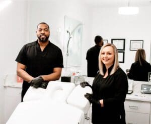 Two people standing in a room with some black gloves on