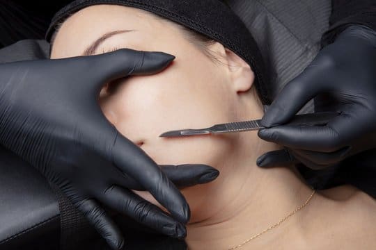 A woman getting her face waxed by two hands.