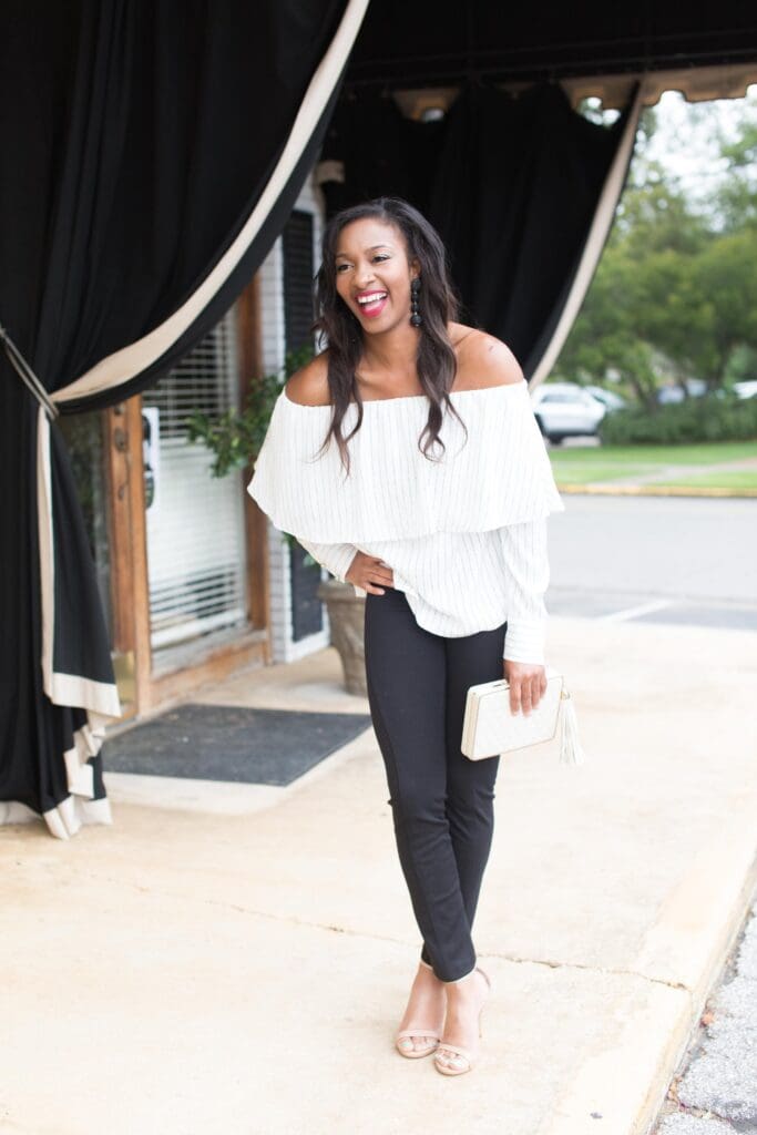 A woman in black pants and white top holding a purse.