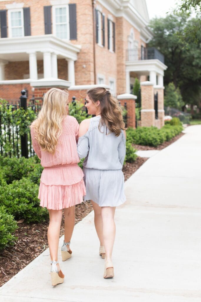 Two women walking down a sidewalk near some bushes.