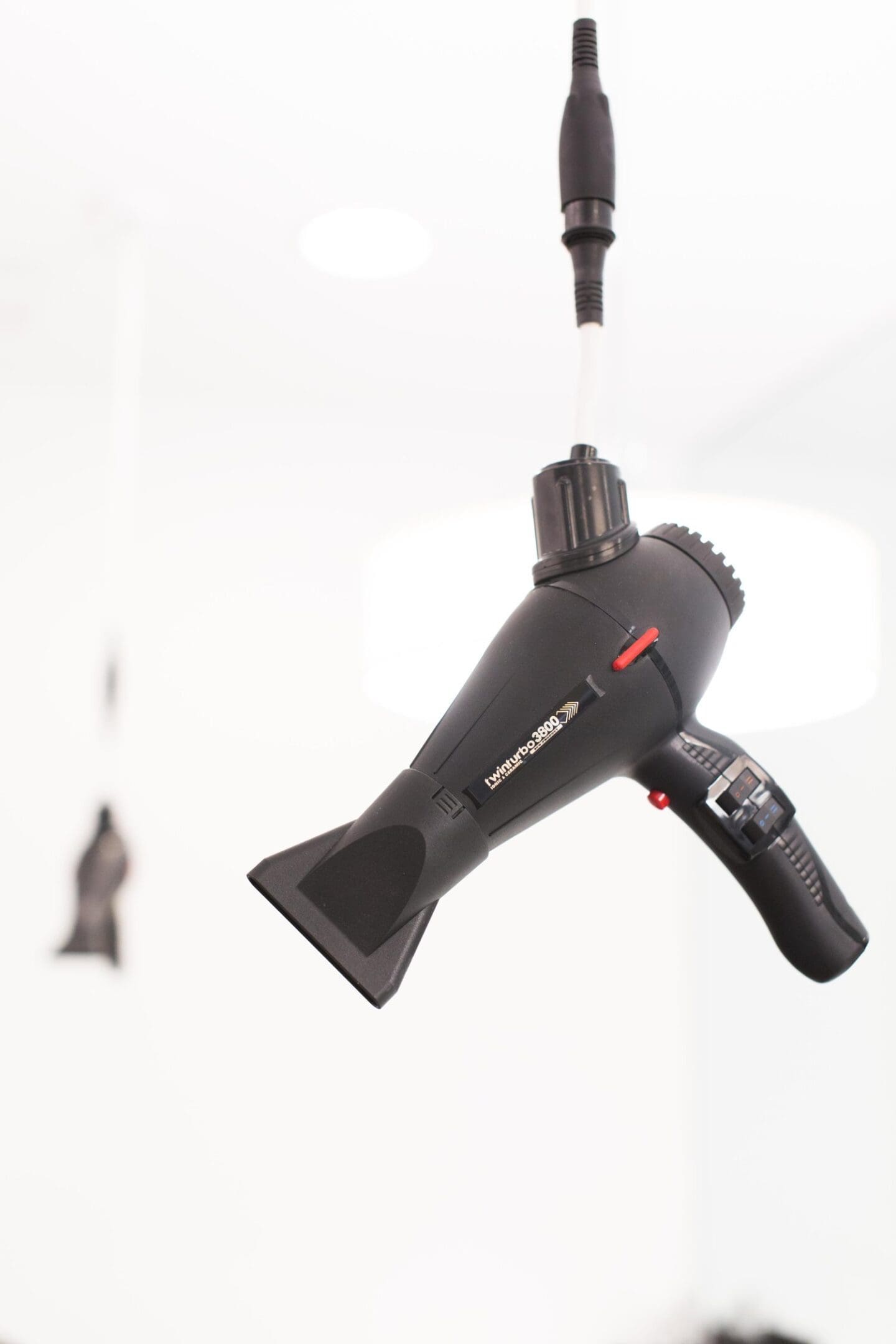 A hair dryer hanging from the ceiling in front of a white wall.