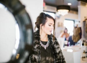 A woman in black shirt and fur coat near mirror.