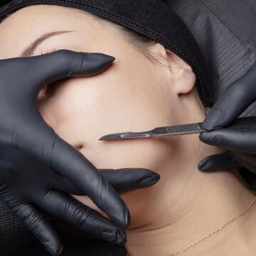 A woman getting her face waxed by two hands.