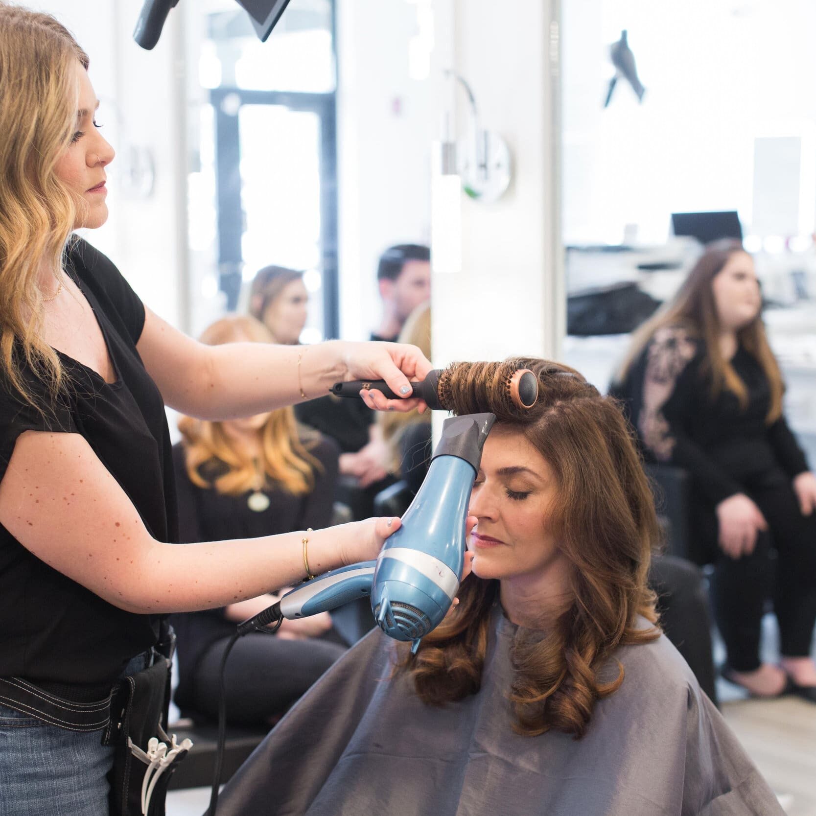 A woman blow drying another woman 's hair.