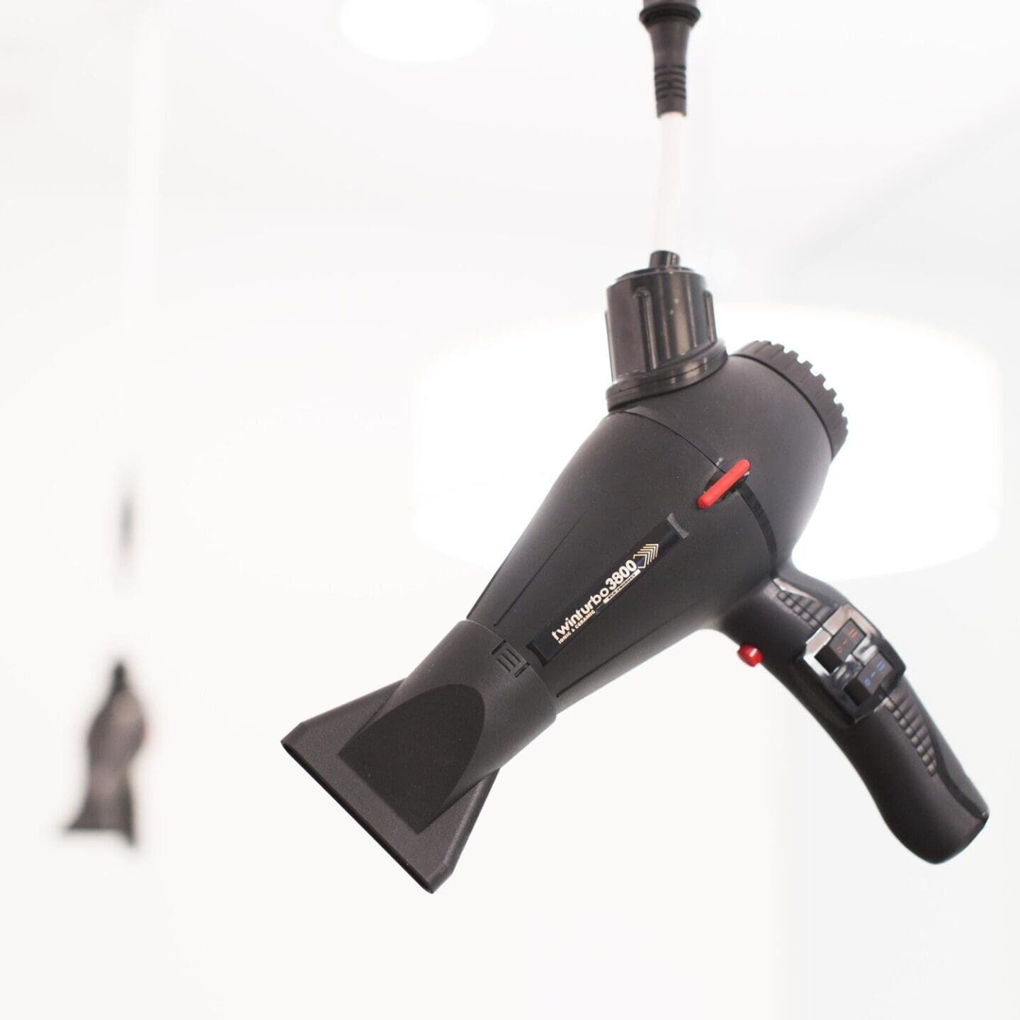 A hair dryer hanging from the ceiling in front of a white wall.