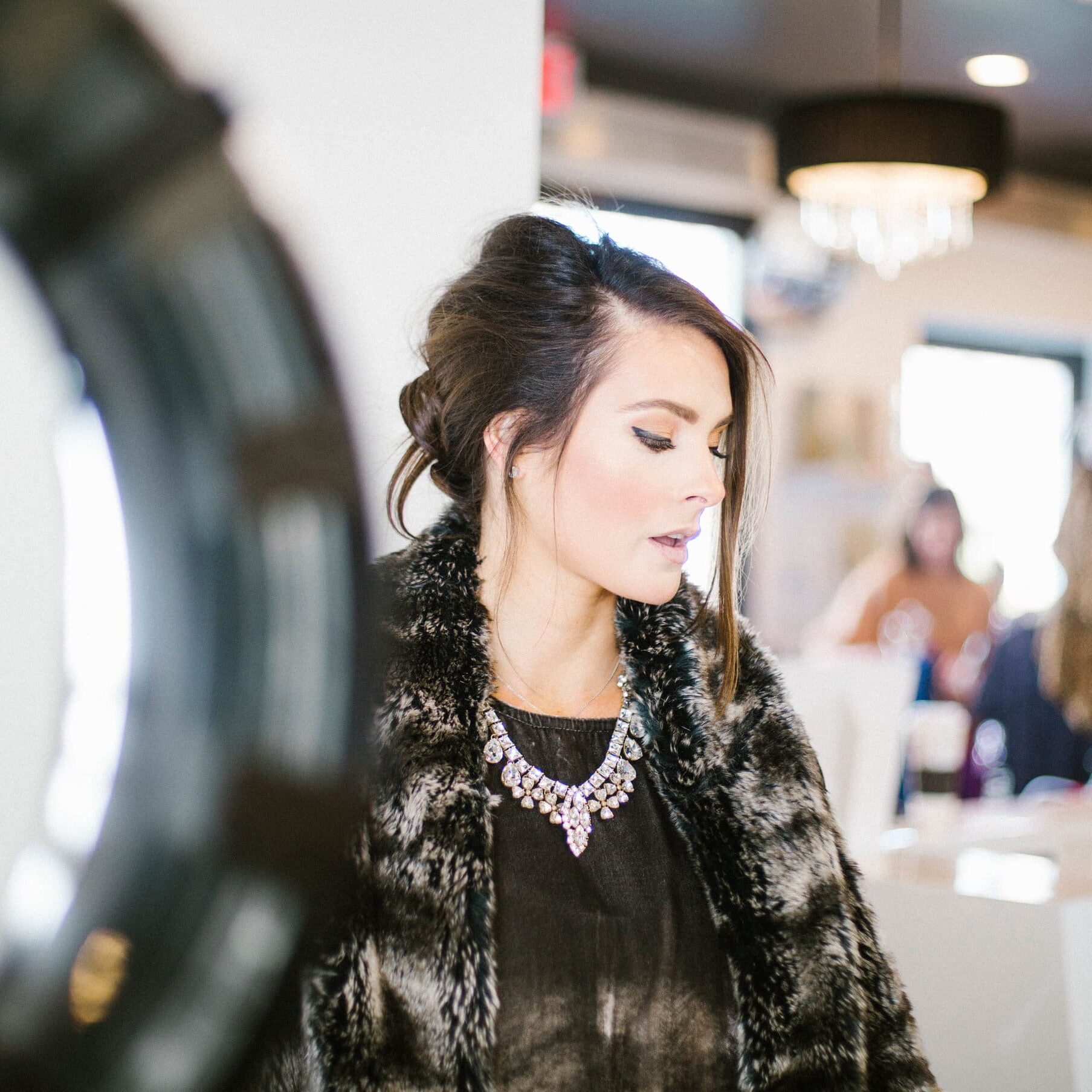 A woman in black shirt and fur coat near mirror.